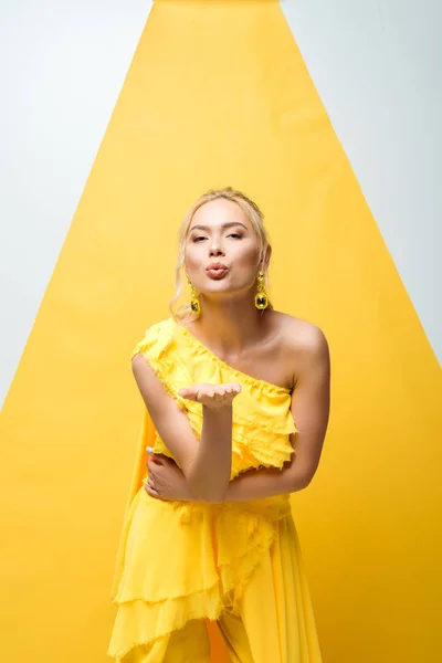 Pretty young woman with duck face sending air kiss on white and yellow — Stock Photo