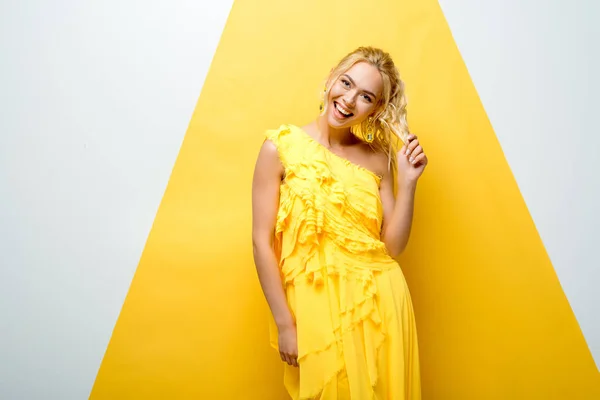 Happy blonde girl touching hair while posing on white and yellow — Stock Photo