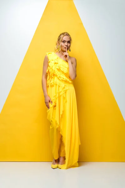 Attractive young woman looking at camera and showing hush sign on white and yellow — Stock Photo