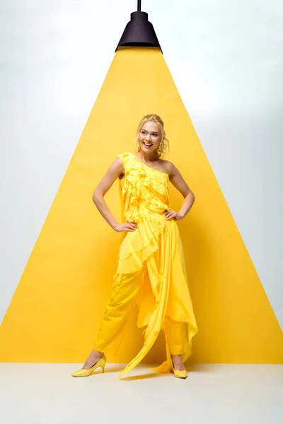 Heureuse jeune femme debout avec les mains sur les hanches et souriant sur blanc et jaune — Photo de stock