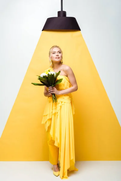 Attrayant jeune femme tenant bouquet de fleurs sur blanc et jaune — Photo de stock