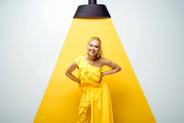 Jovem mulher positiva olhando para a câmera e de pé com as mãos nos quadris em branco e amarelo — Fotografia de Stock
