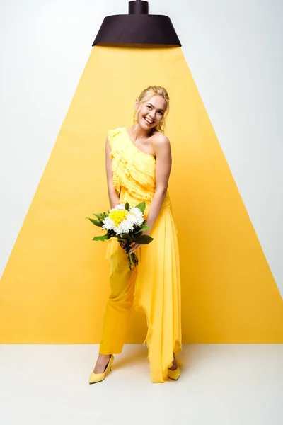 Jeune femme positive tenant bouquet de fleurs sur blanc et jaune — Photo de stock