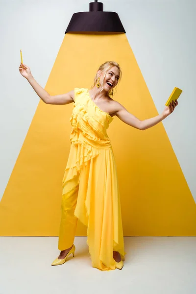 Feliz joven mujer mirando el cuaderno mientras sostiene el lápiz en blanco y amarillo - foto de stock