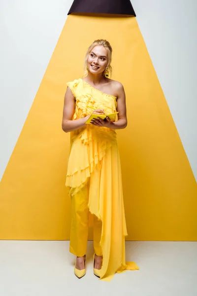 Happy young woman posing and holding notebook with pencil on white and yellow — Stock Photo