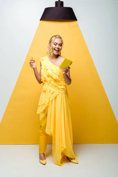 Allegra giovane donna guardando notebook mentre tiene la matita su bianco e giallo — Foto stock