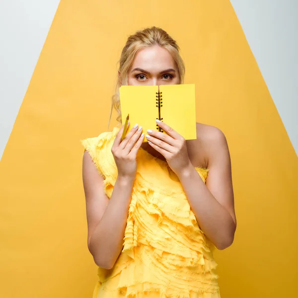 Mujer joven cubriendo la cara con cuaderno en blanco y amarillo - foto de stock