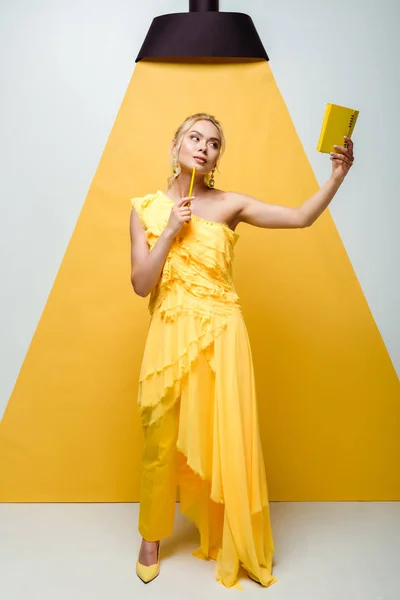 Donna bionda pensierosa che guarda il taccuino mentre posa su bianco e giallo — Foto stock