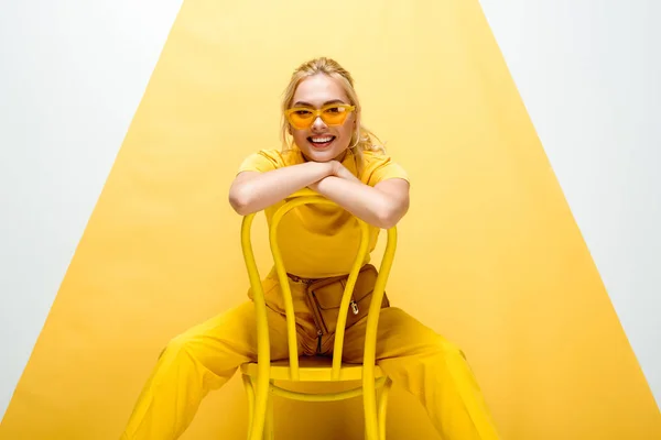 Mujer rubia alegre en gafas de sol sentado en la silla en blanco y amarillo — Stock Photo