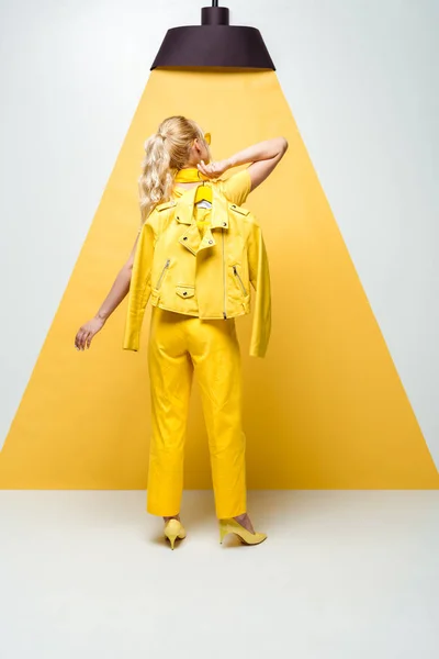 Back view of blonde woman posing and holding hanger with jacket on white and yellow — Stock Photo