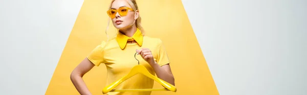 Panoramic shot of attractive woman in sunglasses holding hanger on white and yellow — Stock Photo