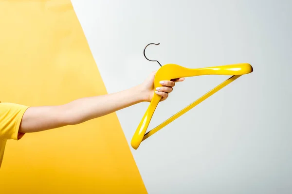 Cropped view of young woman holding wooden hanger on white and yellow — Stock Photo