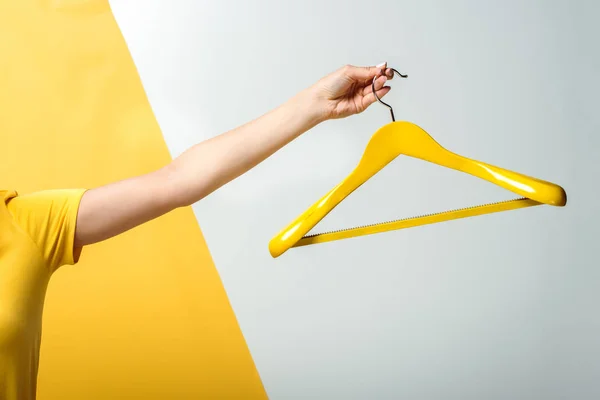 Cropped view of woman holding wooden hanger on white and yellow — Stock Photo