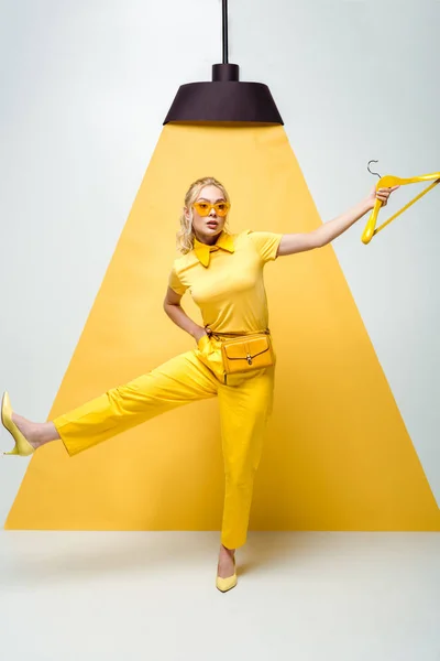 Attractive blonde woman in sunglasses holding hanger and posing on white and yellow — Stock Photo