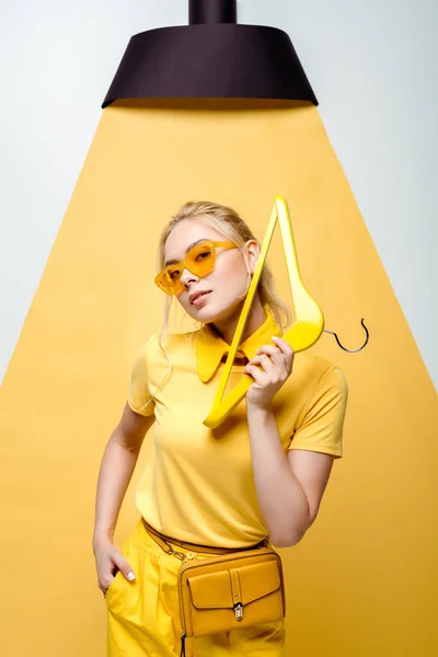 Mulher loira atraente com a mão no bolso segurando cabide e posando em branco e amarelo — Fotografia de Stock