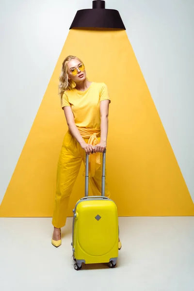 Belle femme en lunettes de soleil posant près des bagages sur blanc et jaune — Photo de stock