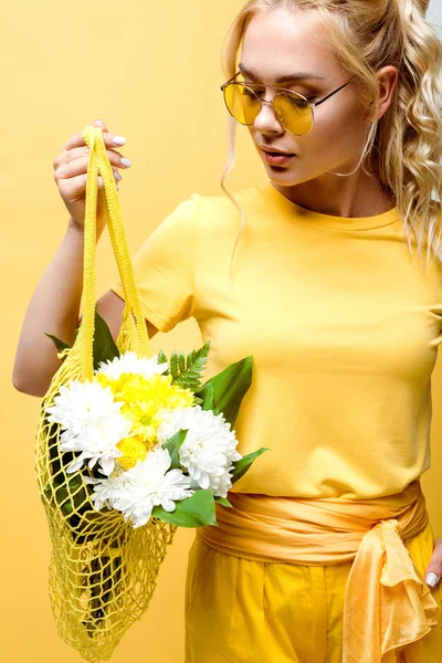 Attractive young woman holding string bag with flowers isolated on yellow — Stock Photo