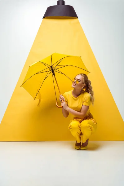 Щаслива блондинка тримає парасольку, сидячи на білому і жовтому — стокове фото