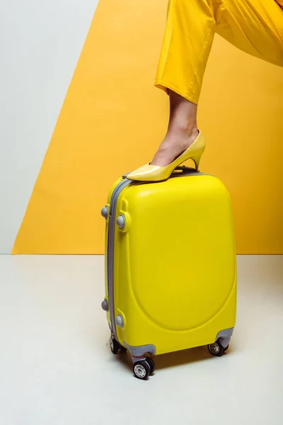 Обрізаний вид стильної жінки, що стоїть на валізі на білому і жовтому — стокове фото