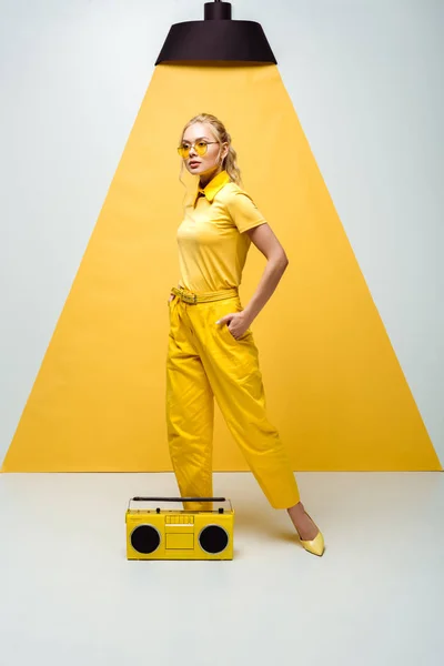 Стильна жінка позує з рукою в кишені біля ретро бумбоксу на білому і жовтому — стокове фото