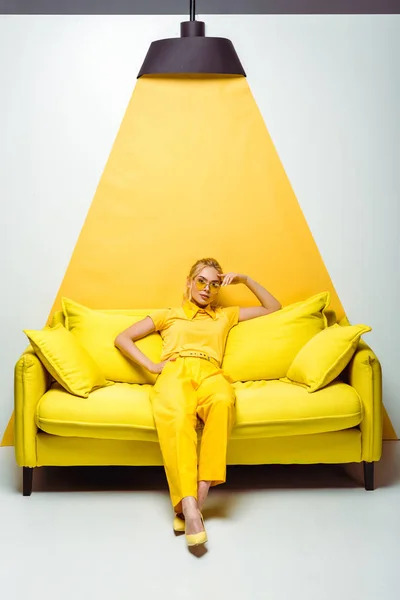 Mulher loira atraente sentado no sofá e olhando para a câmera em branco e amarelo — Fotografia de Stock