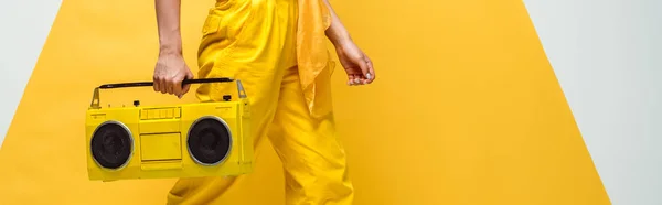 Panoramic shot of young woman holding retro boombox on white and yellow — Stock Photo