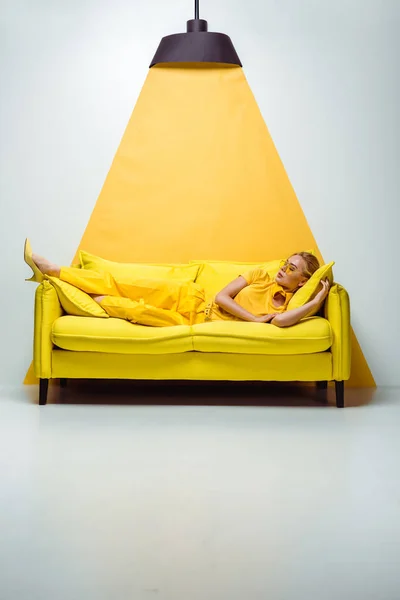 Belle femme en lunettes de soleil couchée sur canapé sur blanc et jaune — Photo de stock