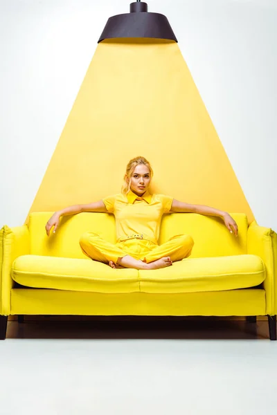 Chica rubia sentada en el sofá con los pies descalzos en blanco y amarillo - foto de stock