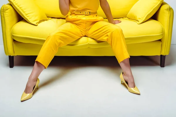Vista recortada de la mujer joven con estilo en tacones sentados en el sofá con almohadas en blanco - foto de stock