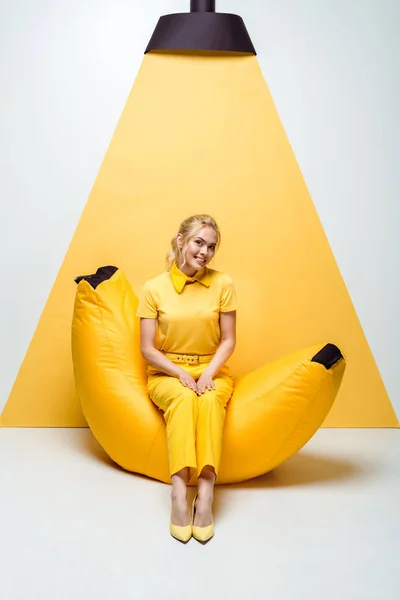 Mulher loira feliz sentada na cadeira de saco de feijão em branco e amarelo — Fotografia de Stock
