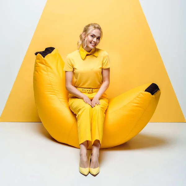 Cheerful blonde woman sitting on bean bag chair on white and yellow — Stock Photo