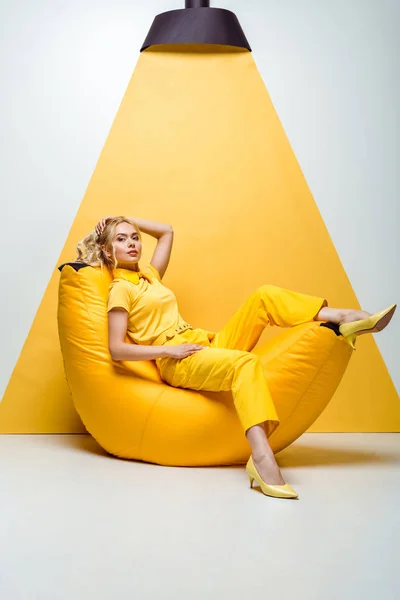 Blondes Mädchen sitzt auf Bean Bag Stuhl und berührt Haare auf weiß und gelb — Stockfoto