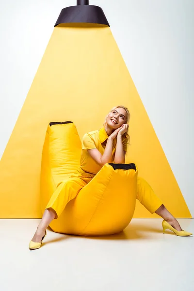 Щаслива блондинка сидить на стільці для мішків на білому та жовтому — Stock Photo
