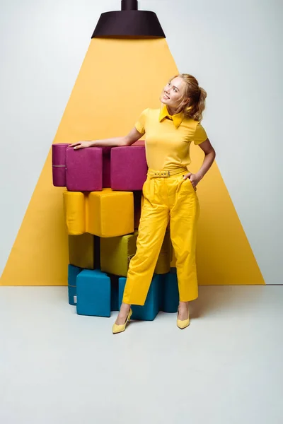 Happy woman posing with hand in pocket near colorful soft puzzle pieces on white and yellow — Stock Photo