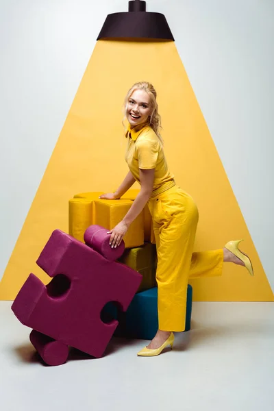 Femme heureuse posant près de pièces de puzzle doux colorés sur blanc et jaune — Photo de stock