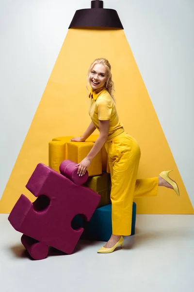 Happy woman posing near colorful soft puzzle pieces on white and yellow — Stock Photo