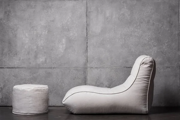 Bean bag chair near white round padded stool on grey — Stock Photo