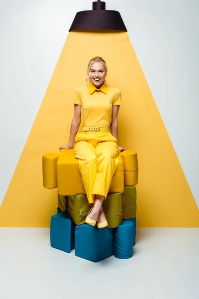 Femme blonde heureuse assise sur de grandes pièces de puzzle doux sur blanc et jaune — Photo de stock