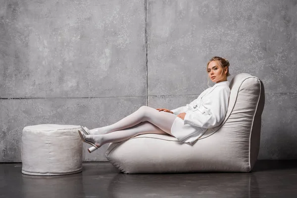 Jolie femme blonde assise sur une chaise de sac de haricot doux sur gris — Photo de stock