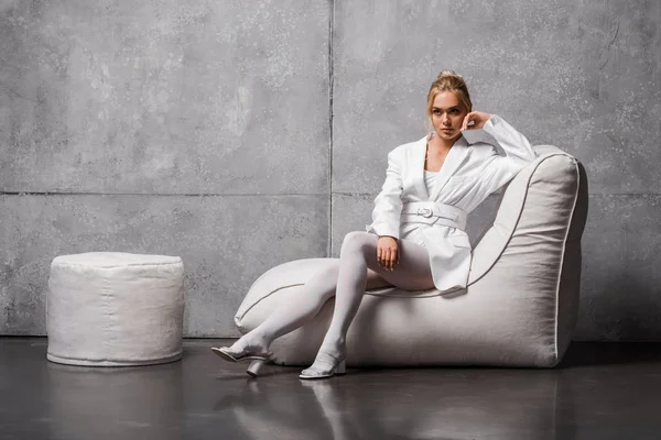 Задумчивая молодая женщина сидит на мягкой фасолью кресло на серый — стоковое фото