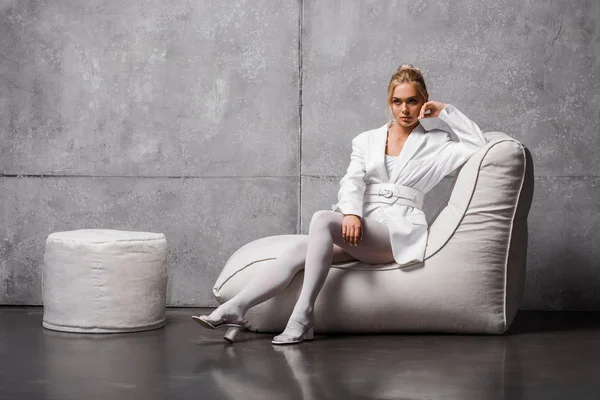 Pensive young woman sitting on soft bean bag chair on grey — Stock Photo