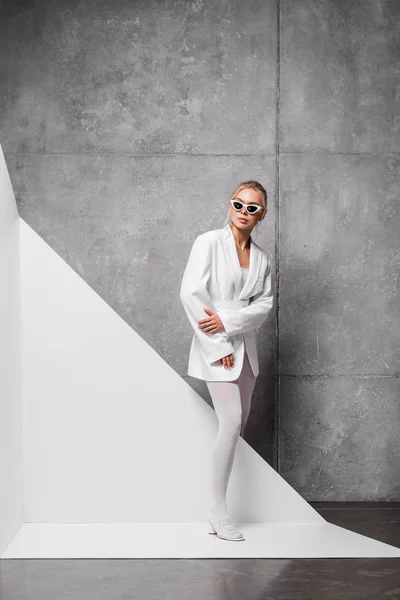 Attraente ed elegante donna in occhiali da sole in posa su bianco e grigio — Foto stock