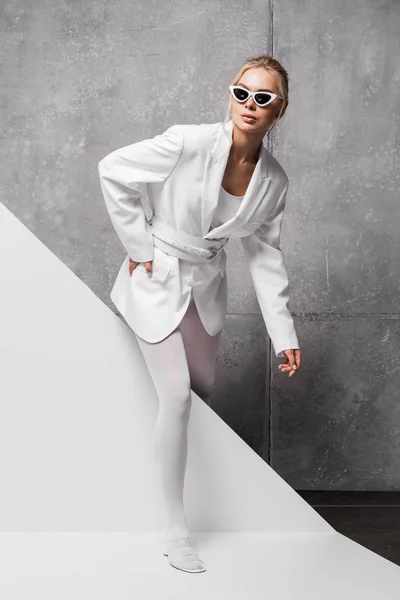 Elegante donna in occhiali da sole in posa con mano in tasca su bianco e grigio — Foto stock