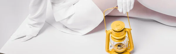 Panoramic shot of young woman sitting with yellow retro lamp on white — Stock Photo