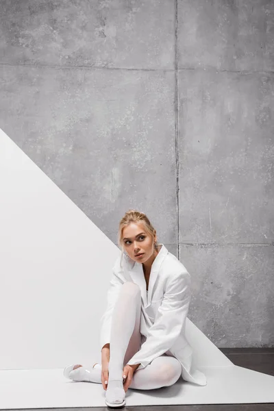 Attractive young blonde woman sitting on white and grey — Stock Photo