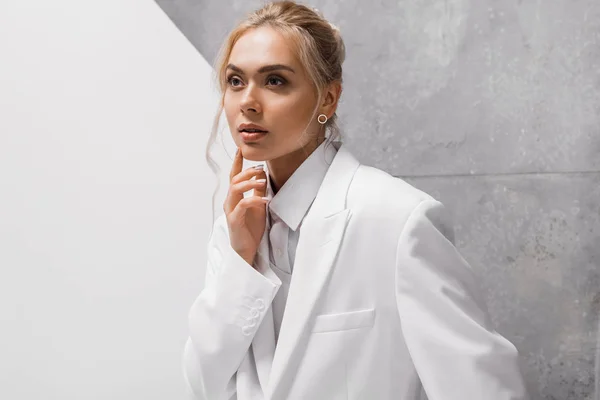 Chère jeune femme blonde touchant menton sur blanc et gris — Photo de stock