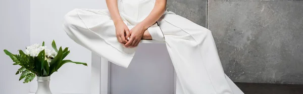 Prise de vue panoramique de la femme élégante assise près du vase avec des fleurs sur blanc et gris — Photo de stock