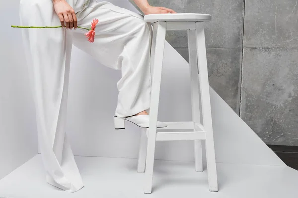Vue recadrée de fille posant près de chaise avec fleur rose sur blanc et gris — Photo de stock