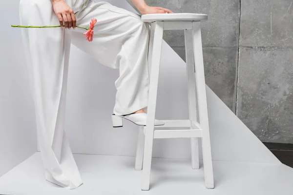 Cropped view of girl posing near chair with pink flower on white and grey — Stock Photo