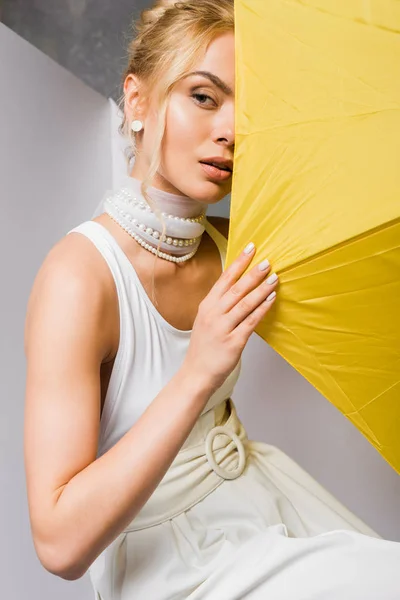 Blonde woman covering face with yellow umbrella on white — Stock Photo